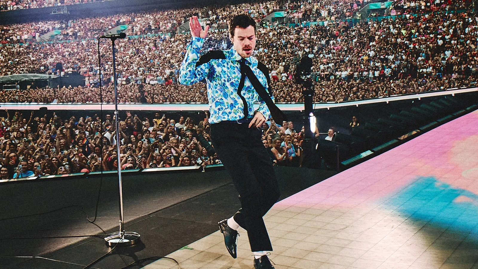 Harry Styles cantando en un escenario con luces y micrófono