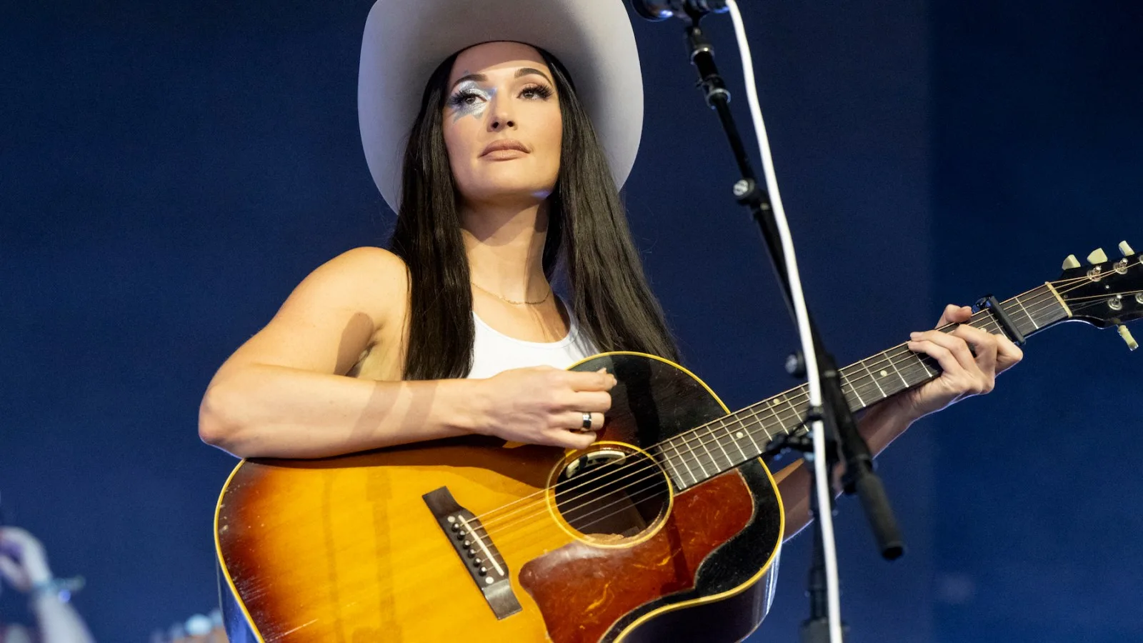 Kacey Musgraves cantando en un escenario con luces cálidas durante un recital